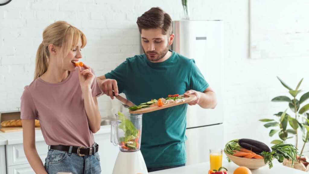 Young couple of vegans preparing vegetable juice at kitchen