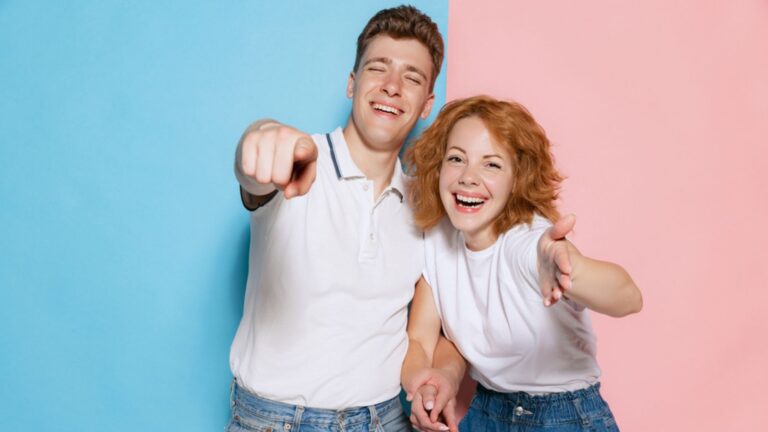 Laughing couple and pointing fingers at camera isolated in blue and pink