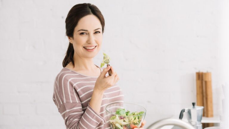 Happy smiling woman looking at camera while eating vegetable salad